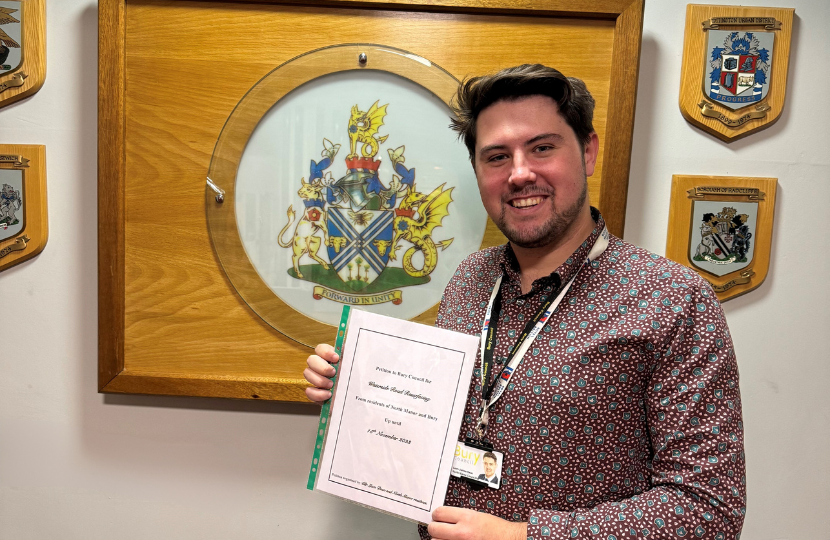 Cllr Liam Dean stands in front of the Bury Coat of Arms with his petition to resurface Waterside Road, Summerseat