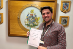 Cllr Liam Dean stands in front of the Bury Coat of Arms with his petition to resurface Waterside Road, Summerseat