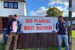 James Daly MP and Cllr Liam James Dean stand in front of the planned mast location with a "Bad Planning Mast Mayhem" sign